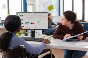 Two coworkers examining charts on a monitor in a modern office.